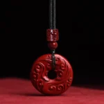 Cinnabar lotus peace buckle pendant necklace with hand-carved cloud patterns on red fabric background, front close-up view