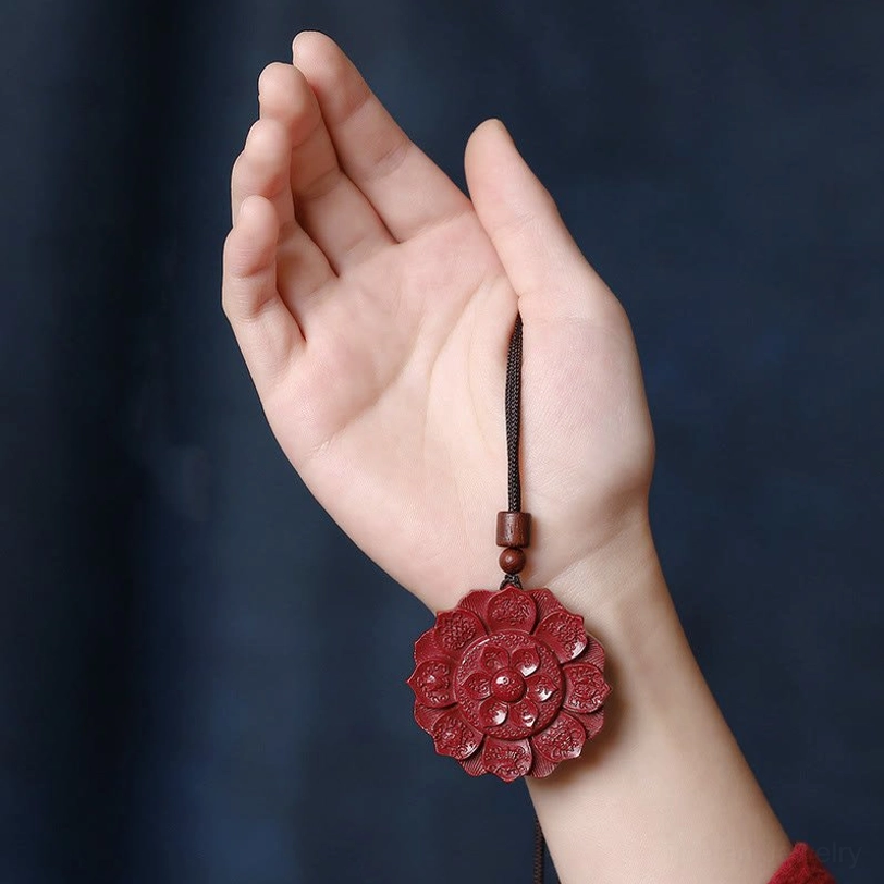 Hand-carved cinnabar lotus pendant held on human palm, showing intricate detail and deep crimson color of the blessing necklace