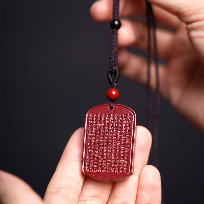 Cinnabar Lotus Heart Sutra necklace flat lay hand view displaying full engraved sutra surface on dark background