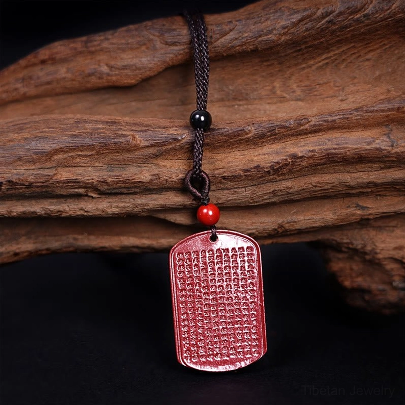 Tibetan Lotus Heart Sutra cinnabar necklace side angle showing carved text and cord against natural wood texture