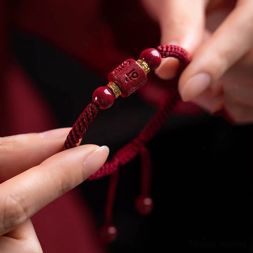 Handwoven cinnabar mantra bracelet held in hand showing braided cord structure, round beads, and dangling adjustment tails - detail close-up