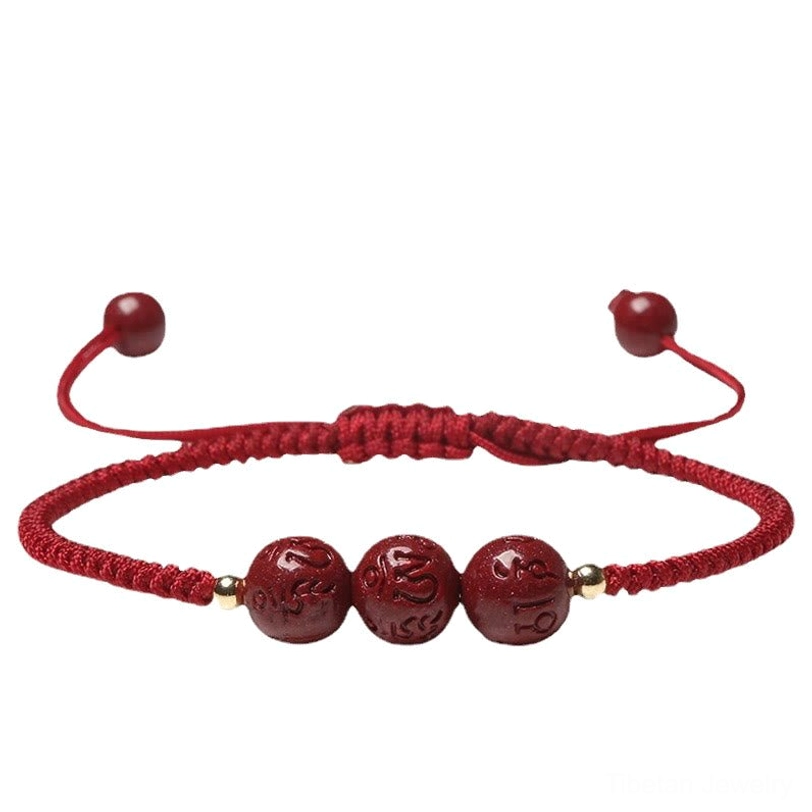 Handcrafted cinnabar meditation bracelet flat lay showing adjustable red cord with three engraved mantra beads on dark wood