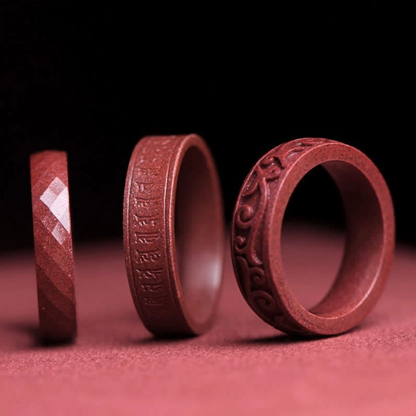 Three handcrafted cinnabar om mani padme hum blessing rings displayed side by side showing faceted, carved, and smooth styles