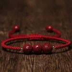 Handmade cinnabar Om Mani Padme Hum engraved red string bracelet flat lay top view with dark red beads on wooden background