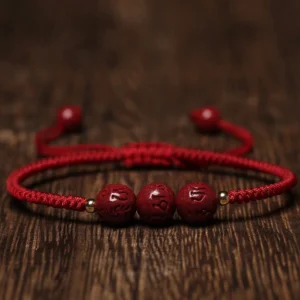 Handmade cinnabar Om Mani Padme Hum engraved red string bracelet flat lay top view with dark red beads on wooden background