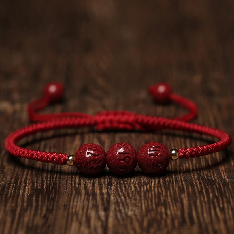 Handmade cinnabar Om Mani Padme Hum engraved red string bracelet flat lay top view with dark red beads on wooden background