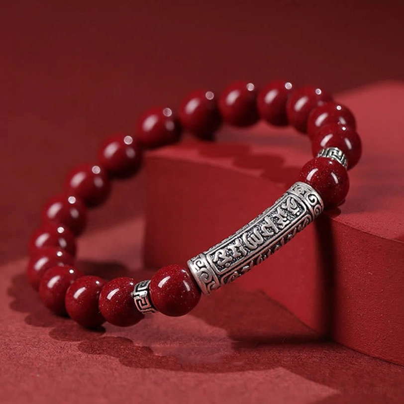 Cinnabar Six True Words bracelet low three-quarter view on red geometric display blocks showing glossy beads and detailed engraved silver tube