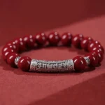 Cinnabar Six True Words blessing bracelet top-down view showing deep red matte cinnabar beads with engraved sterling silver Om Mani Padme Hum charm tube