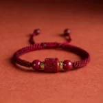Handwoven Cinnabar Om Mani Padme Hum Tibetan blessing bracelet with wine-red braided cord and engraved mantra bead - front flat view showing adjustable pull knot closure