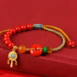 Cinnabar peace buckle blessing bracelet flat lay showing red cinnabar beads, orange agate, green spacers, and gold-braided blue rope with peace buckle pendant