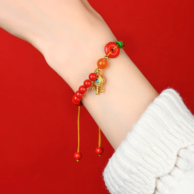 Tibetan cinnabar peace buckle bracelet worn on wrist with white knitted sweater cuff showing dangling beads underneath