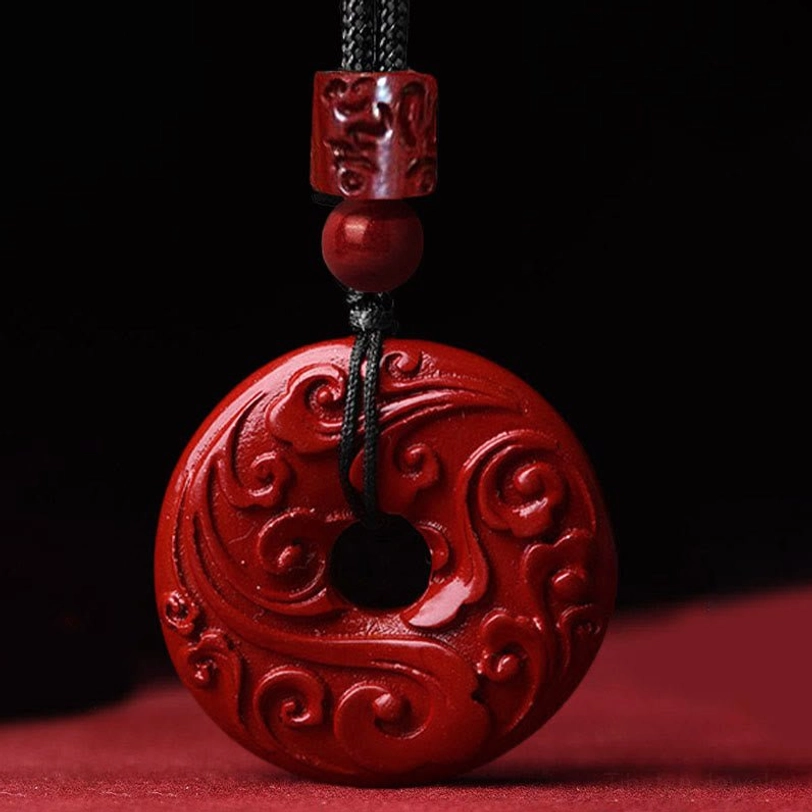 Cinnabar peace buckle pendant with intricate swirling cloud engravings on braided black cord, top-down detail view