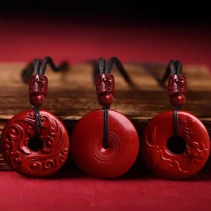 Three cinnabar peace buckle pendant variations showing carved and smooth surfaces on wooden display, flat lay product photography