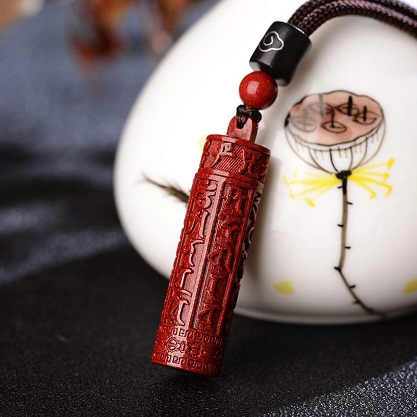 Cinnabar mantra pendant with Tibetan script engraving displayed on ceramic lotus ornament, side view detail