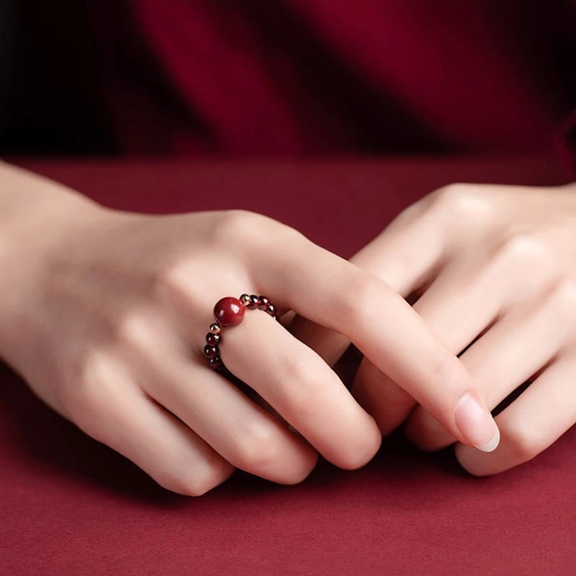 Single cinnabar PiXiu protection ring side view showing adjustable beaded band with large crimson center charm and gold spacers