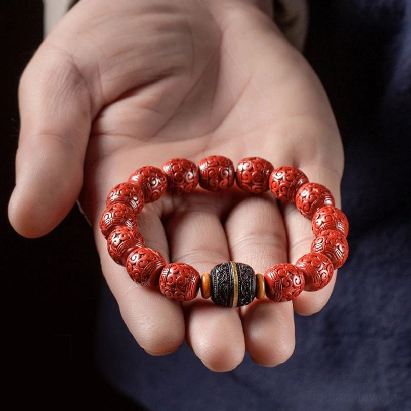 Close-up hand-held view of cinnabar ebony bracelet with red carved beads and black spacer components against dark blue background