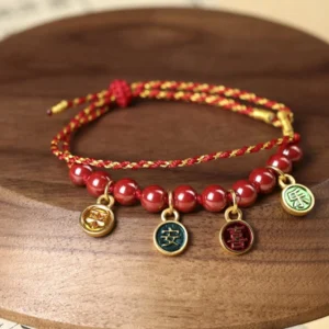 Cinnabar red string blessing bracelet with gold-tone charms displayed on wooden tray, showing intricate braided weave and natural beads