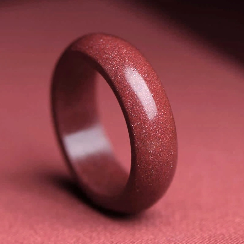 Close-up side view of polished cinnabar blessing ring showing deep reddish-brown granular texture and natural sparkle