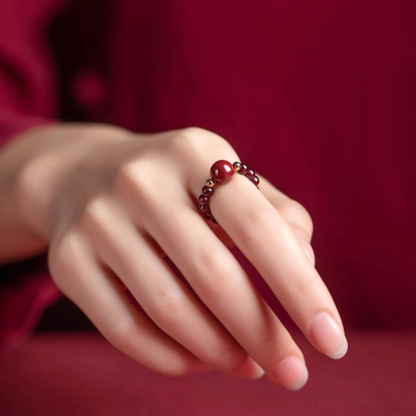 Cinnabar round bead ring with prominent center stone and precious metal details, eye-level side view on wine red fabric
