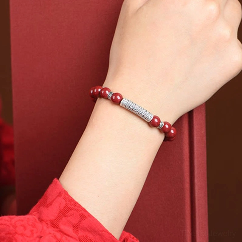 Cinnabar Om Mani Padme Hum bracelet worn on wrist close-up showing slim comfortable fit with red beads and silver charm