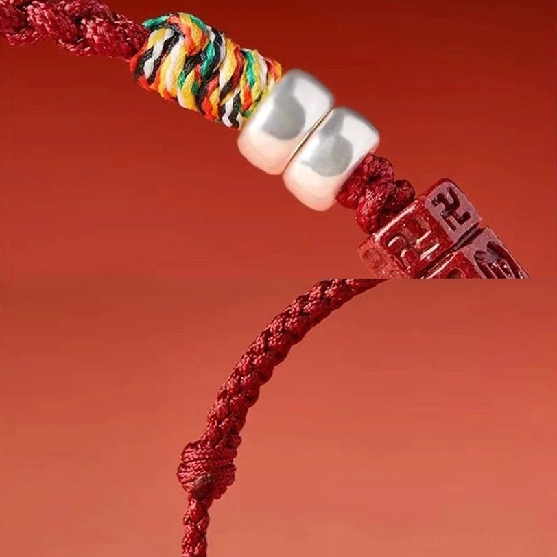 Macro close-up of sterling silver and carved cinnabar charm on red blessing cord bracelet