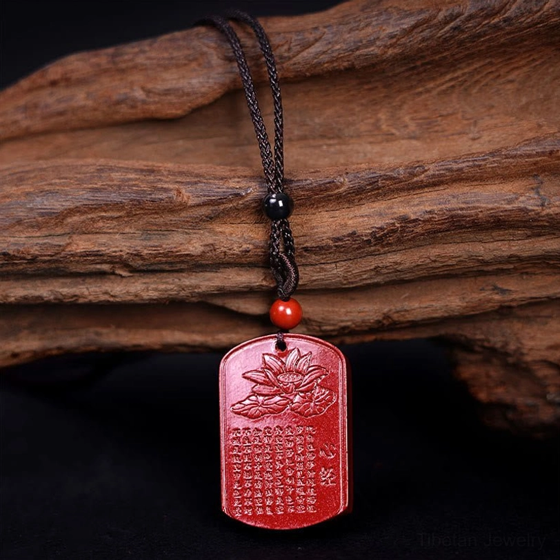 Cinnabar pendant necklace side view showing engraved Heart Sutra text and woven black cord with red accent bead on natural bark background