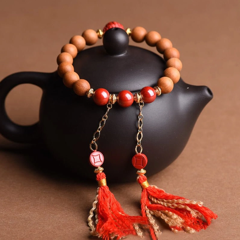 Tibetan tassel bracelet three-quarter view with tan wood beads, red cinnabar beads, and dual red silk tassels on decorative wooden tray