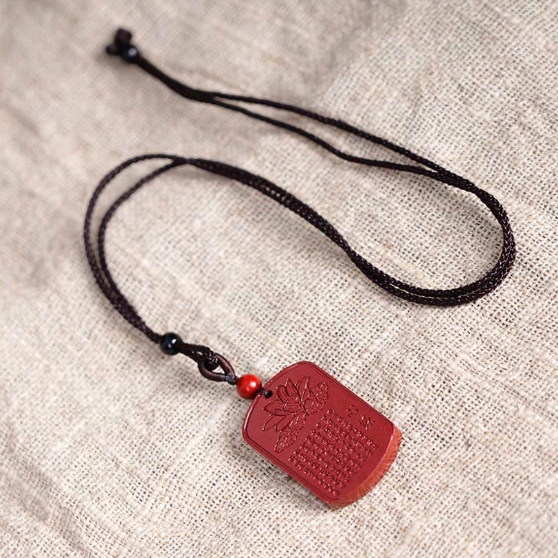 Tibetan cinnabar lotus Heart Sutra necklace flat lay on linen fabric showing complete cord and pendant arrangement
