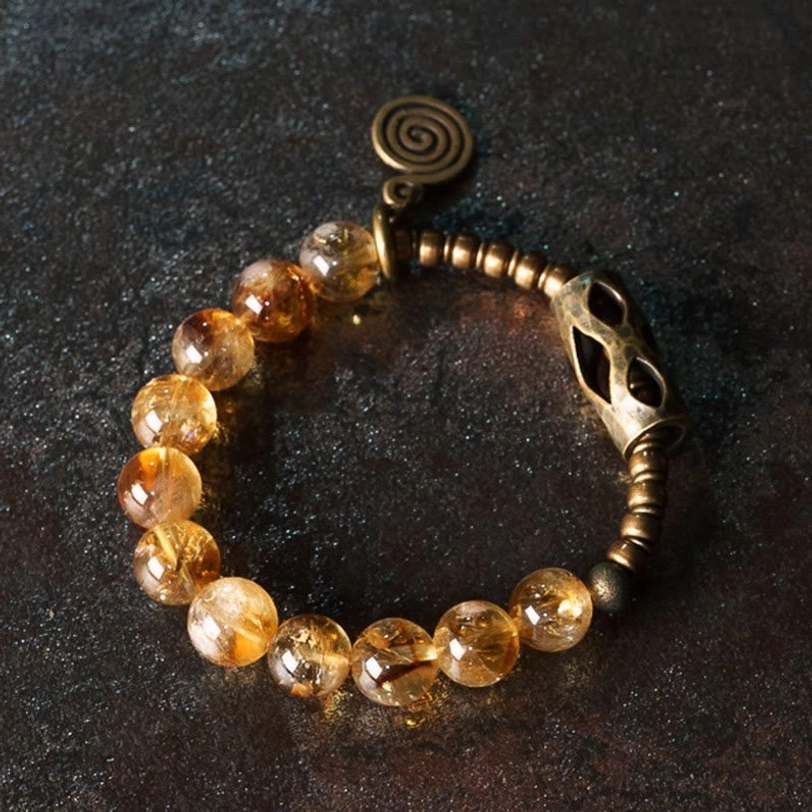 Citrine bead bracelet detail showing spiral metal charm and carved brass spacer beads on elastic string