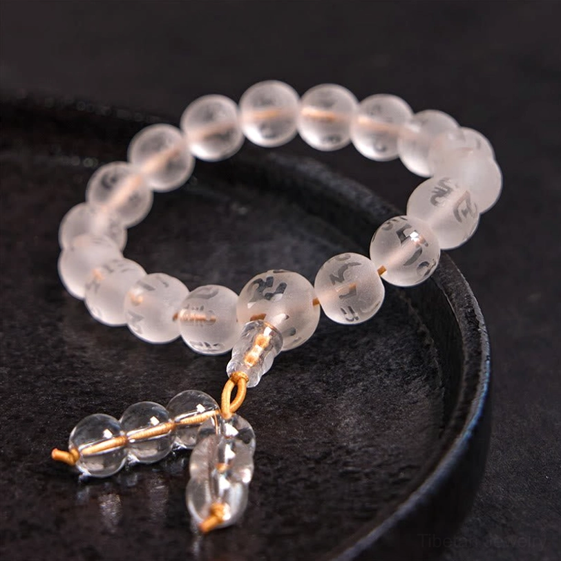 Clear quartz prayer bracelet with engraved mantra beads and gold hardware tassel on black ceramic tray