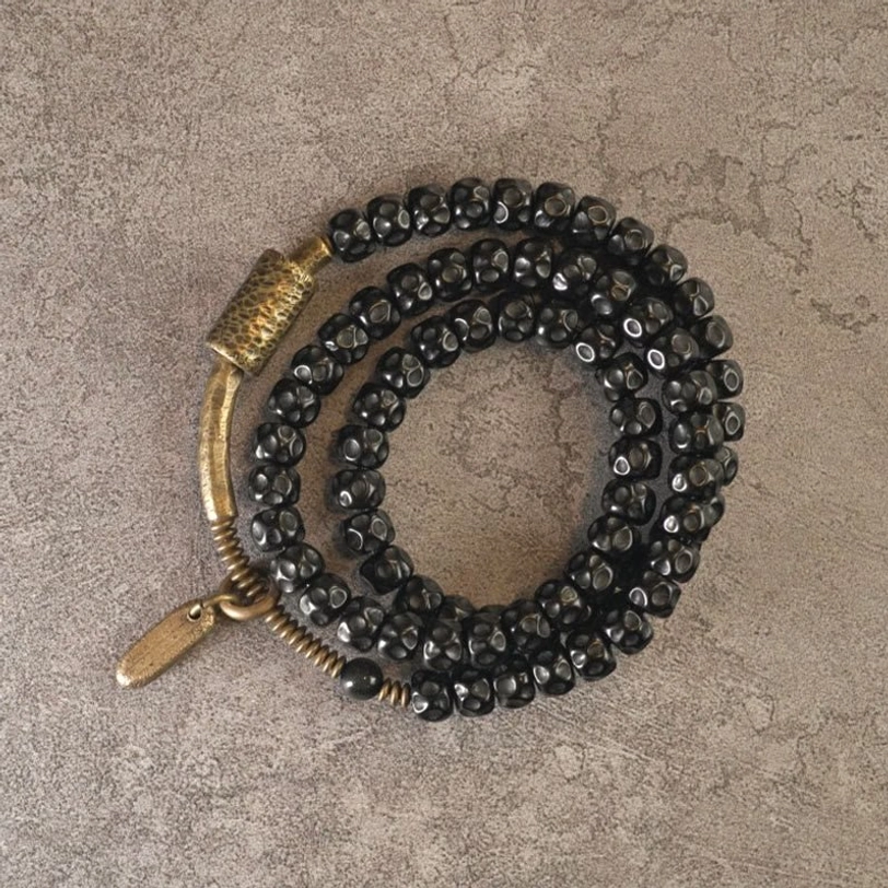Angled top-down view of coconut shell triple wrap bracelet - curved brass accent piece with metal tag pendant