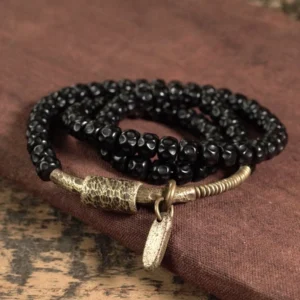Triple wrap coconut shell beaded bracelet top-down view on burgundy fabric - black faceted beads with vintage brass accents