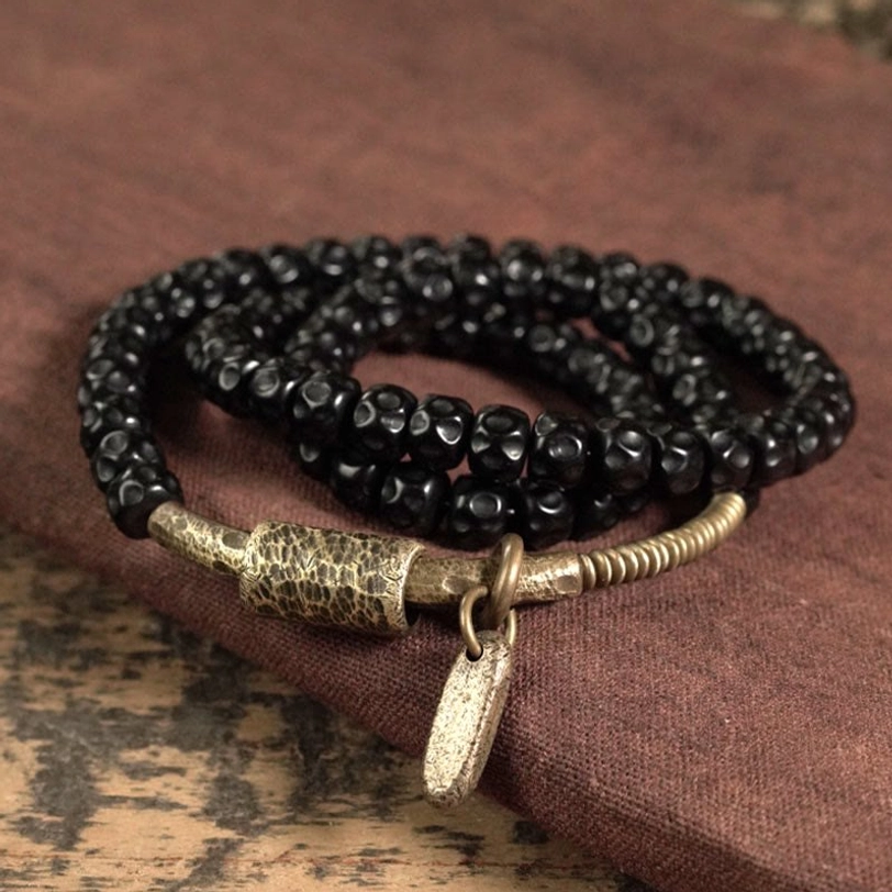 Triple wrap coconut shell beaded bracelet top-down view on burgundy fabric - black faceted beads with vintage brass accents