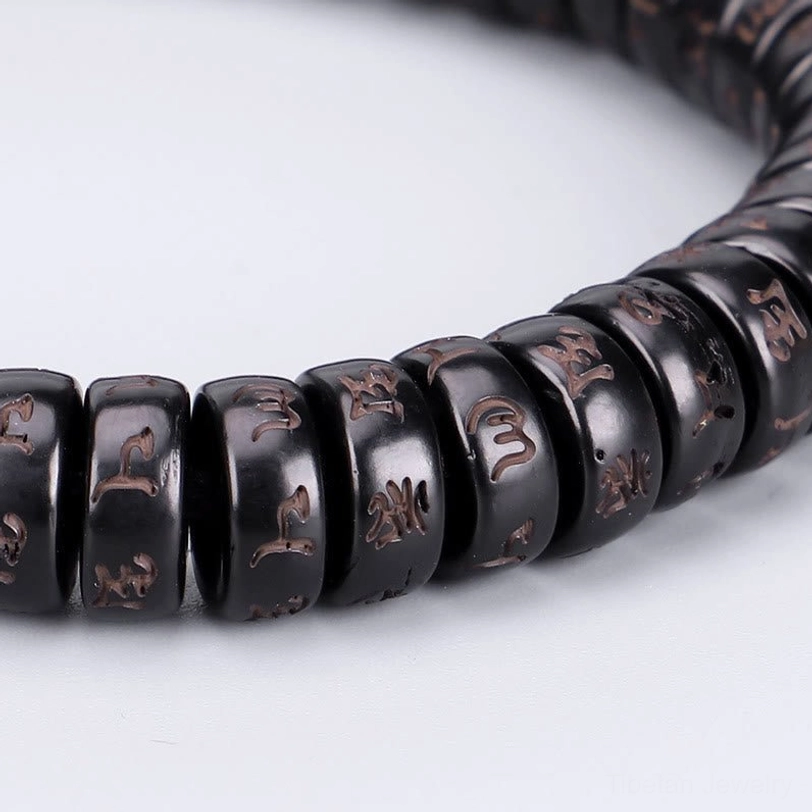 Close-up macro detail of engraved Tibetan coconut shell beads showing clear sacred mantra inscriptions and bead texture