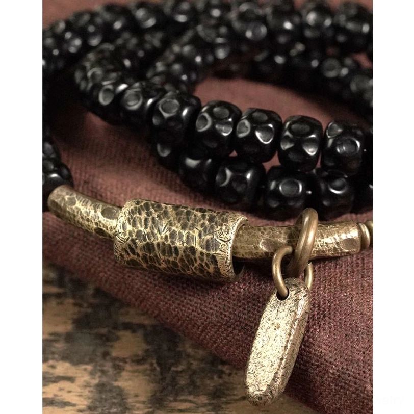 Close-up detail view of coconut shell bracelet with hammered brass accent and metal tag pendant on burgundy fabric
