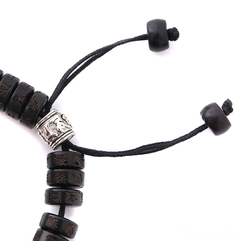Close-up macro shot of Tibetan prayer bracelet showing engraved silver beads, intricate craftsmanship, and black drawstring stoppers