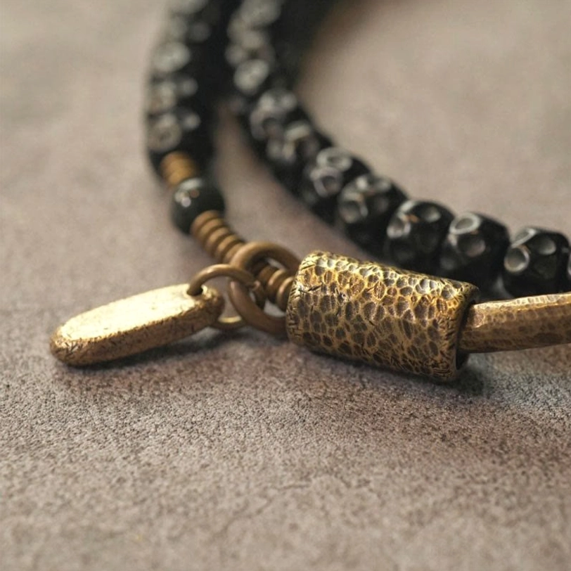 Macro close-up of coconut shell bracelet components - textured brass tube, black faceted beads, and metal tag detail