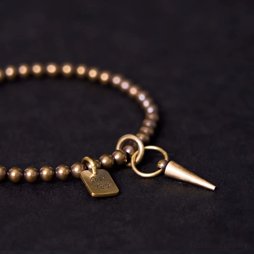 Oblique close-up of handcrafted copper bracelet showing round bead texture and dual charm structure