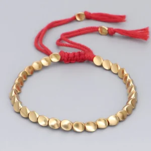 Red cord copper bead bracelet with tassel detail, oval matte copper beads and knotted adjustable closure on studio background