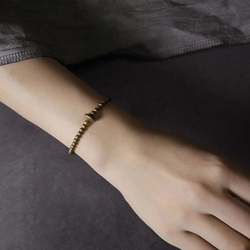 Side profile of slim elasticated copper bracelet worn on arm showing dainty bronze metal design on fabric background