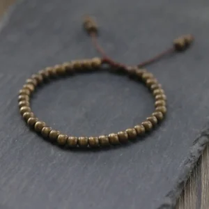 Flat lay of handmade copper beads bracelet with decorative knot closure and tassel detail on stone and wood background