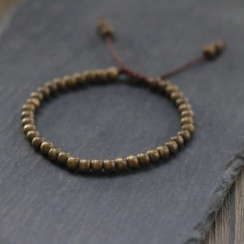 Flat lay of handmade copper beads bracelet with decorative knot closure and tassel detail on stone and wood background