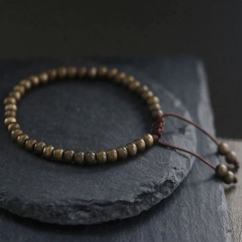 Three-quarter side view of adjustable copper brass beads bracelet showing bronze round beads and braided pull cords
