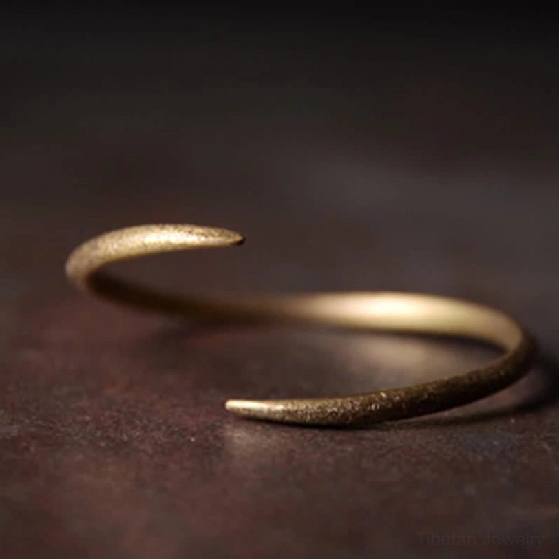 Single copper claw cuff bracelet side view, mixed smooth and textured gold sections, adjustable open design on wooden backdrop