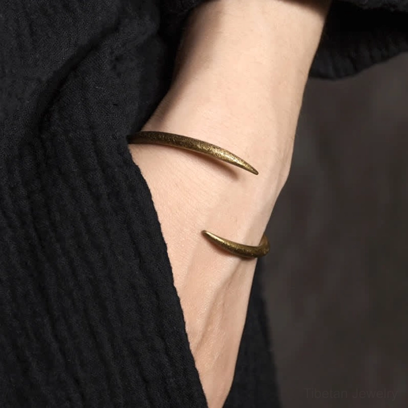 Dual copper claw cuff bracelets worn on wrist, aged gold tone, lifestyle close-up showing adjustable open design on black linen
