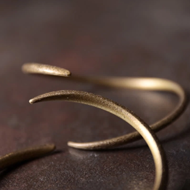 Stacked copper claw cuff bracelets layered together, bronze-gold matte finish, overlapping curved claw designs on wooden surface