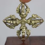 Authentic handcrafted copper double dorje vajra held in hand, top-down close-up view showing intricate 5-prong cross design with carved scroll details