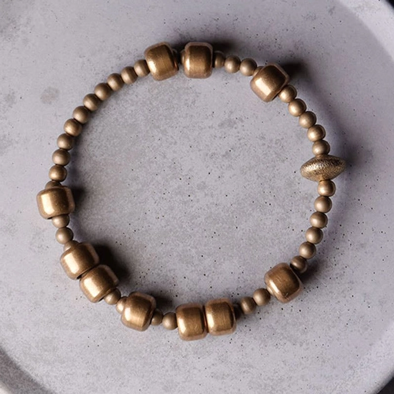 Full display of vintage copper brass bracelet with asymmetrical barrel bead design on light ceramic surface