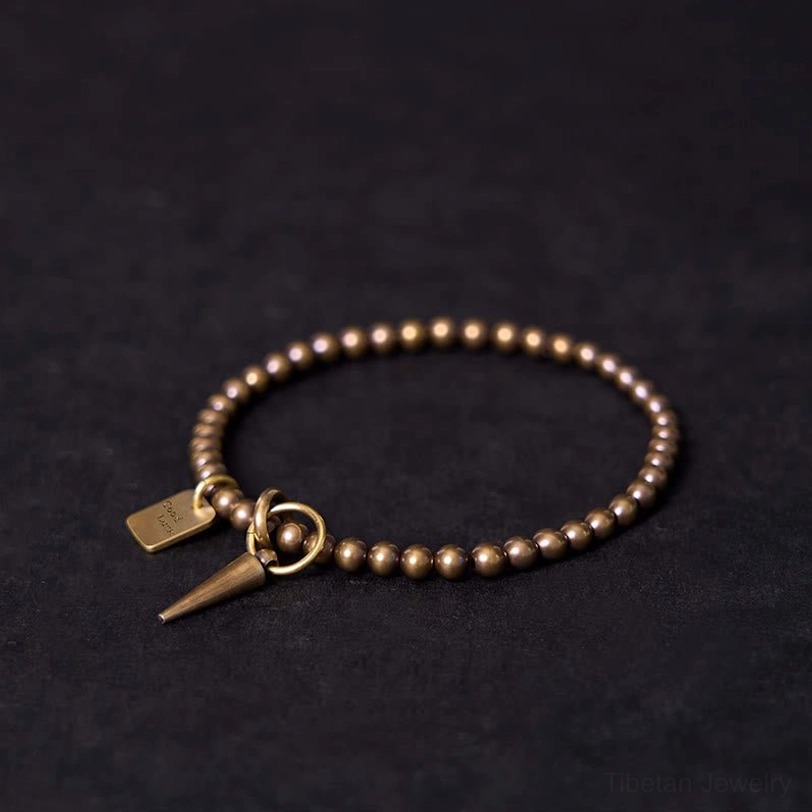 45-degree angle view of antique copper beaded bracelet with geometric spike pendant and engraved charm