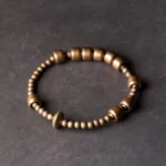 Vintage copper brass wealth bracelet with barrel and round beads in warm antique bronze, displayed overhead on grey background